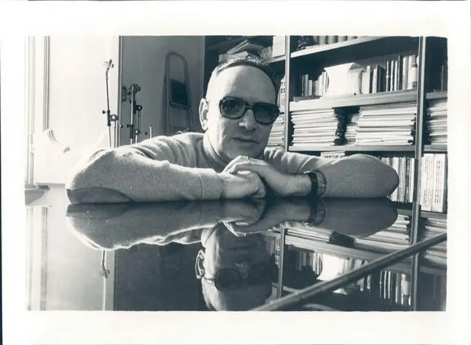 A black and white image of Morricone in the 1960s, posing over a piano.