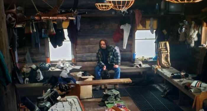 Russell Crow as John Biebe in Mystery, Alaska (1999). Screen capture off Amazon. Hollywood Pictures/Buena Vista Pictures Distribution. Local star recently kicked off the hockey team, John Biebe sits in the locker room alone having an existential crisis.