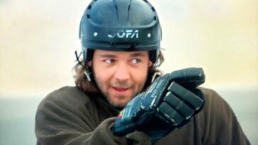 Russell Crow as John Biebe in Mystery, Alaska (1999). Screen capture off Amazon. Hollywood Pictures/Buena Vista Pictures Distribution. John Biebe out on the ice playing hockey, pointing to a teammate as if to say well done.