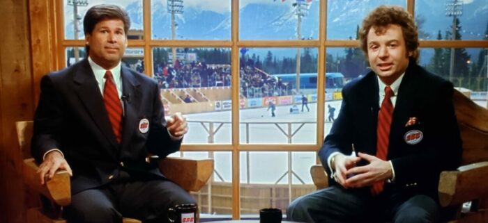 Jim Fox and Mike Myers as Jim Fox and Donnie Shulzhoffer in Mystery, Alaska (1999). Screen capture off Amazon. Hollywood Pictures/Buena Vista Pictures Distribution. Hockey commentators in a wood paneled studio.