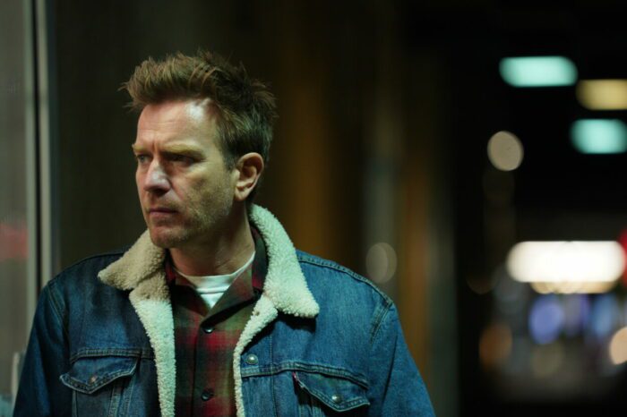 Ewan McGregor as Father in Bleeding Love (2023). Image courtesy of R&CPMK. Father in his fur lined denim jacket, strolling the motel parking lot.