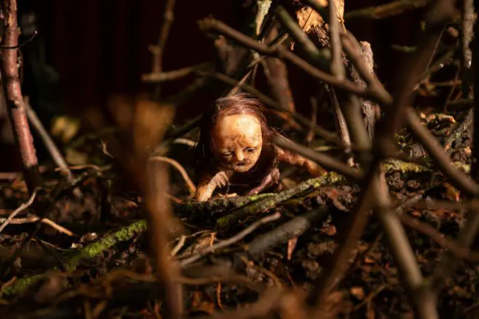 Image from STOPMOTION depicting a peculiar figure crawling through a thick, dark forest. 