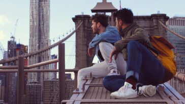 Aeneas and Alex sit on a rooftop and look at the city skyline.