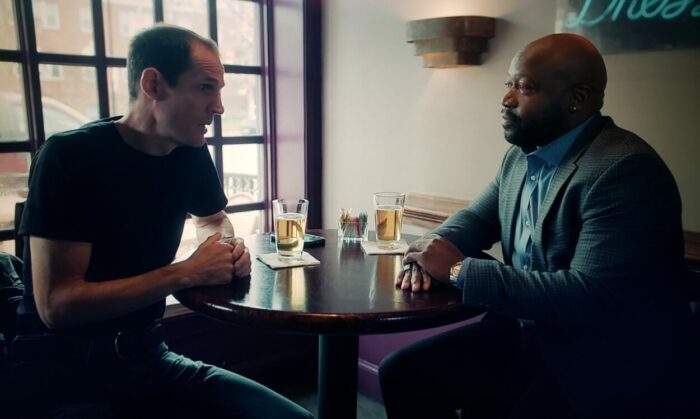 Joey Collins and Marcellus Bassman Shepard as Jack and David in There is a Monster (2024). Screen capture off of Vimeo. Two men in a bar drinking pints of beer.