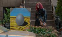(L-R) Julio Torres, Tilda Swinton as Alejandro and Elizabeth in Problemista (2024) Credit: Jon Pack. Courtesy of A24. Magenta haired Elizabeth stands beside young Alejandro who is holding up a painting of an egg.