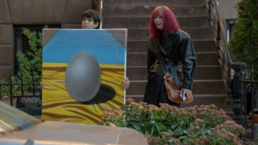 (L-R) Julio Torres, Tilda Swinton as Alejandro and Elizabeth in Problemista (2024) Credit: Jon Pack. Courtesy of A24. Magenta haired Elizabeth stands beside young Alejandro who is holding up a painting of an egg.