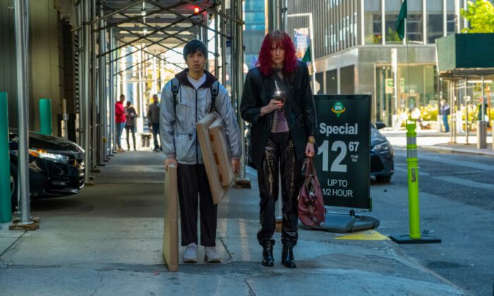 (L-R) Julio Torres, Tilda Swinton as Alejandro and Elizabeth in Problemista (2024) Credit: Jon Pack. Courtesy of A24. Young man carrying wrapped canvas paintings walking alongside an eccentricity dressed woman on a city street.