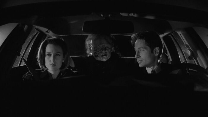 Scully (Gillian Anderson) and Mulder (David Duchovny), drive as the Creature (Chris Owens) rides in the back seat.