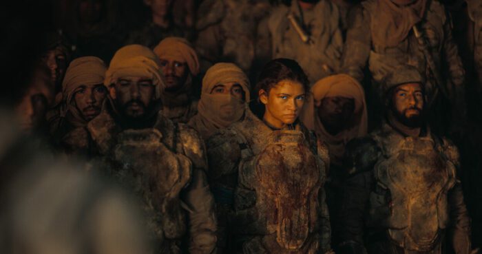 ZENDAYA as Chani in Warner Bros. Pictures and Legendary Pictures’ action adventure “DUNE: PART TWO,” a Warner Bros. Pictures release. (PRESS KIT). © 2024 Warner Bros. Entertainment Inc. All Rights Reserved. Photo Credit: Courtesy of Warner Bros. Pictures. Chani standing among Fremen in their typical wraps and desert gear, glaring at displeasing events unfolding.