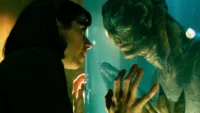 Sally Hawkins with Doug Jones as the amphibian man in The Shape of Water. They're both pressing their hands to the glass tank wall between them.