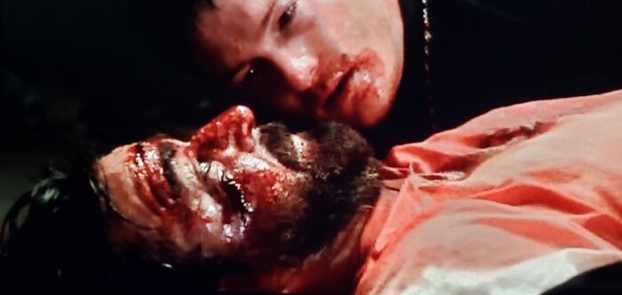 Norman Reedus and David Della Rocco as Murphy and Rocco in The Boondock Saints (1999). Screen capture off of DVD. Franchise Pictures. Connor lays beside a bloody Rocco who is dying of a gunshot wound.