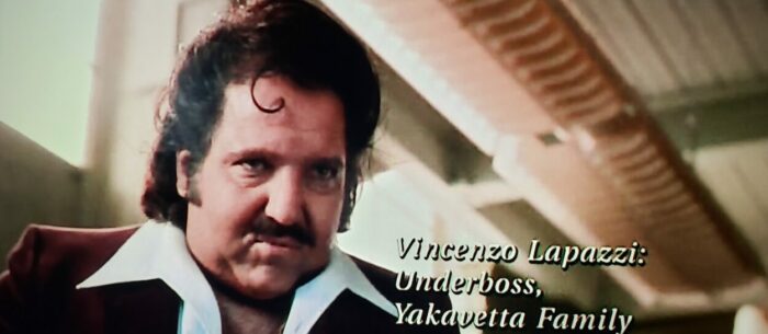 Ron Jeremy as Vincenzo Lapazzi in The Boondock Saints (1999). Screen capture off of DVD. Franchise Pictures. Looking like a sleazy lounge singer, mafia underboss Lapazzi glares down while info about him is printed on screen.