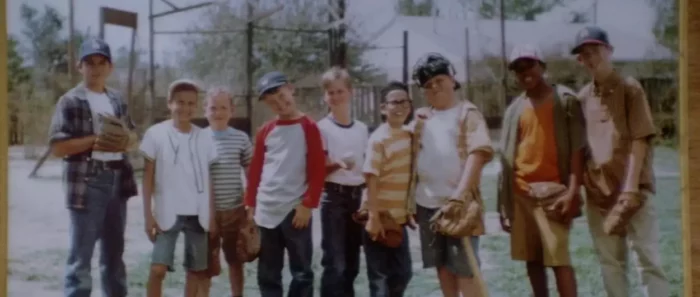 The boys from The Sandlot are dressed in their summer attire and smiling at the camera in the 1960's sandlot baseball field