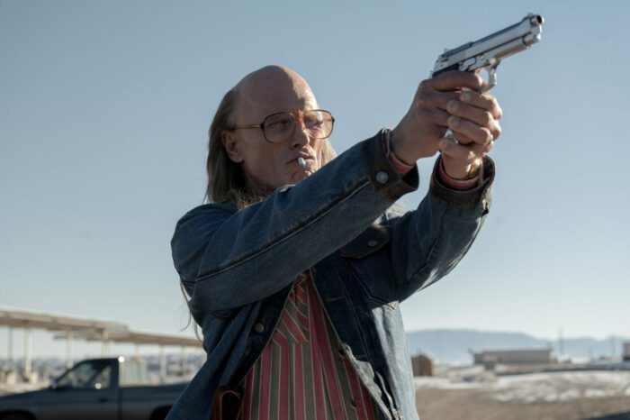 Lou Sr. (Ed Harris), smoking a cigarette, aims his gun in the distance and is about to shoot in Love Lies Bleeding