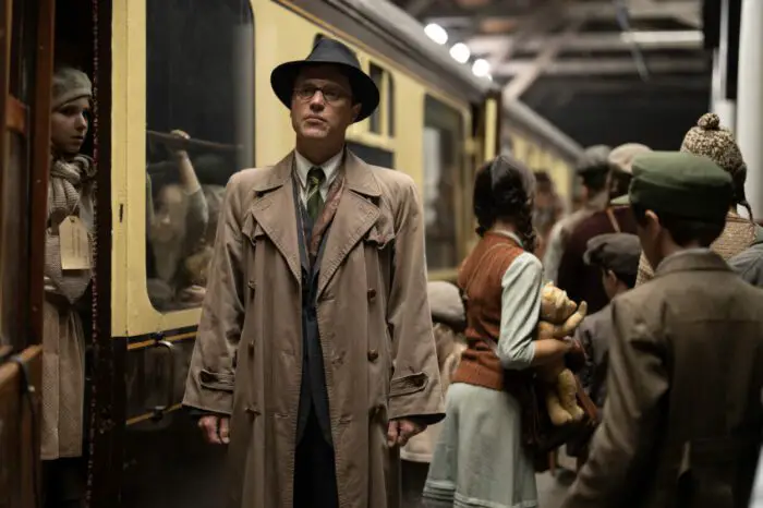 A man in an overcoat and hat stands on a train platfrom