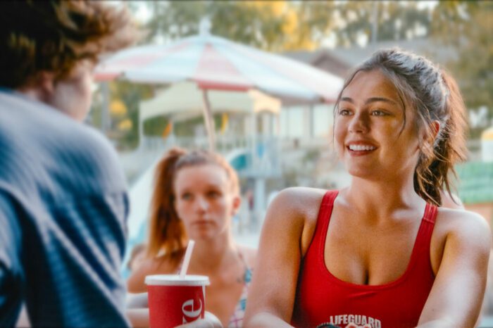Lifeguard Brooke wears a bright red bathing suit and meets A.J. for the first time at the poolside Snack Shack. 