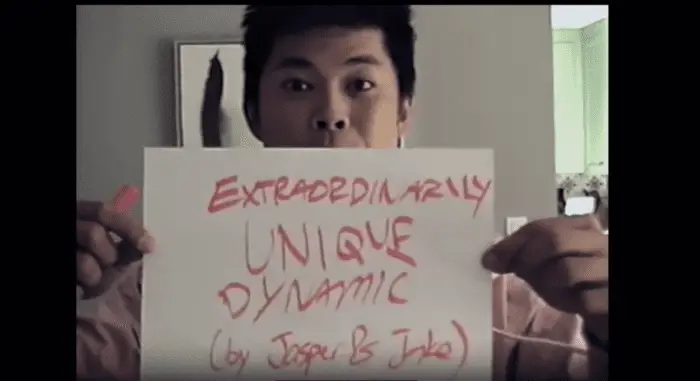 Ryan, in character, holds up a handwritten sign that says, "Extremely Unique Dynamic"