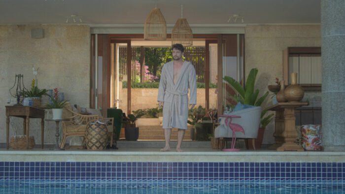 David (Jacson Rathbone), wearing a robe, inspects the pool of the property he has inherited.