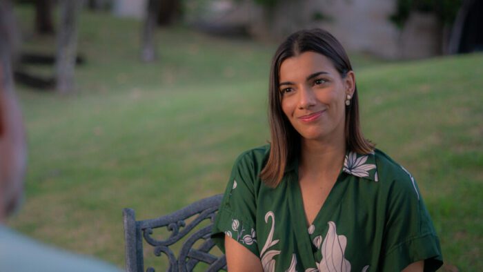 Raquel (Clara Lago), wearing a forest green dress, smiles.