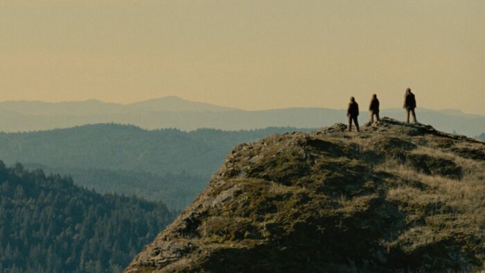 Three Sasquatches stand on a mountain overlooking the wilderness