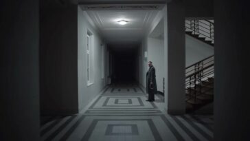 Rudolf Höss (Christian Friedel) stands at the edge of a hallway, witnessing a glimpse of his true legacy in the future.