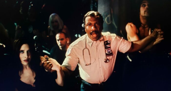 Ving Rhames and Charis Michelsen among others as Marcus and I. B. Bangin’s girlfriend in BRINGING OUT THE DEAD (1999). Screen capture off of Amazon. Paramount Pictures. Marcus assembles club goers in black to perform a prayer over an overdose so he can pretend Jesus rather than Narcan is saving the junkie's life.
