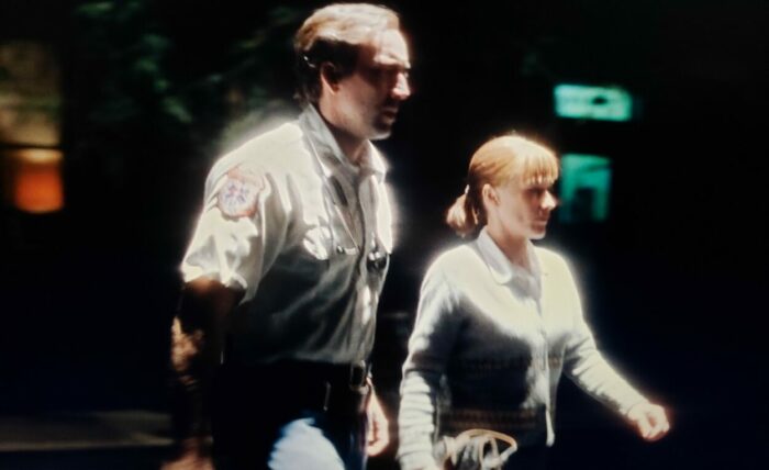 Nicolas Cage and Patricia Arquette as Frank and Mary in BRINGING OUT THE DEAD (1999). Screen capture off of Amazon. Paramount Pictures. Cinematically lit to seem like they're shining in the dark, Mary and Frank cross a dark street during the night.