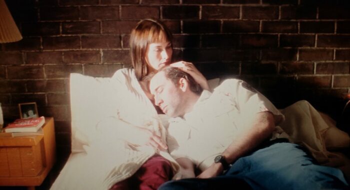 Nicolas Cage and Patricia Arquette as Frank and Mary in BRINGING OUT THE DEAD (1999). Screen capture off of Amazon. Paramount Pictures. Mary and Frank lay in bed together, clothed, as Mary holds Frank and the two are bathed in white light.