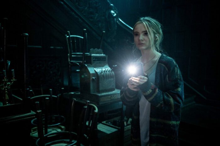 A young woman explores a dark room, using her phone as a flashlight.