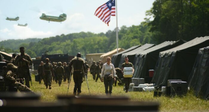 Reporters walk through a makeshift military base as helicopters fly overhead in Civil War.