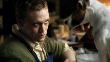 Caleb Landry Jones, seated, looks up and to camera right as Douglas in Dogman.