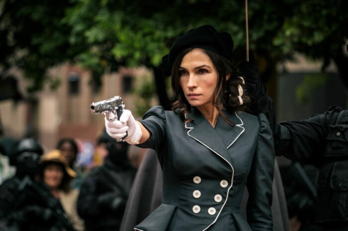 Famke Janssen as Hilda Van Der Koy in Boy Kills World (2024). Courtesy of Roadside Attractions. Despotic ruler Hilda wears a vintage black dress while pointing an automatic pistol covered in baroque etchings.