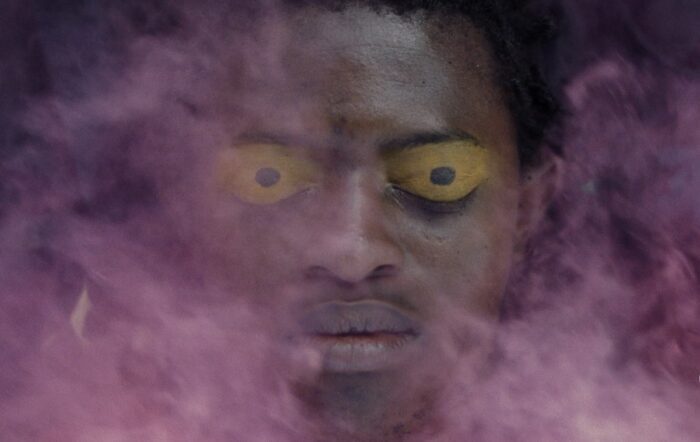 Ethereal image of a man with yellow eyes and shrouded in purple smoke.
