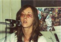 Judee Sill in the documentary Lost Angel: The Genius of Judee Sill. Greenwich Entertainment. Judee Sill singing while wearing lightly tinted sunglasses.