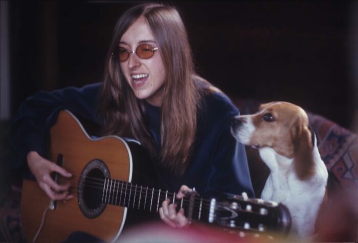 Judee Sill in the documentary Lost Angel: The Genius of Judee Sill. Greenwich Entertainment. Judee Sill playing an acoustic guitar with a dog beside her.