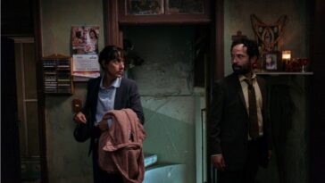 A man and woman, both dressed in business attire, enter a shabby apartment.