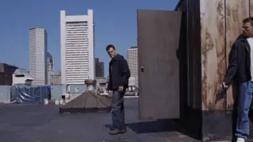 One man with a gun hides from another on a rooftop in The Departed