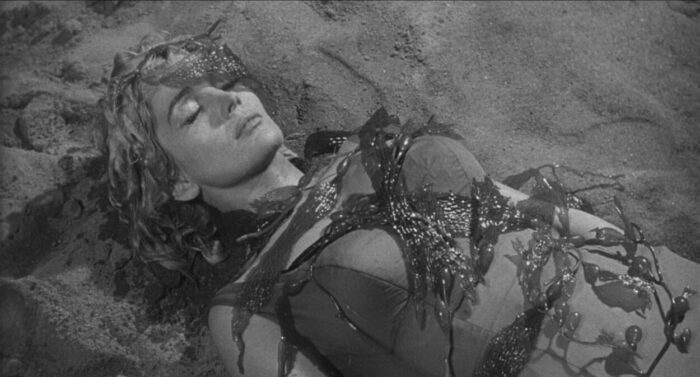 Vi (Juli Reding) lay dead on the beach, her body transforming into seaweed.