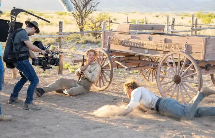 A cinematographer operates the camera as two actors engage in a gunfught on the set of The War Between.