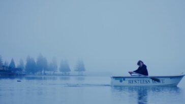 Elijah Carnazzo as Galen in Winter Island. Adventus Films. Galen rows a white boat across the glassy still water of a lake.