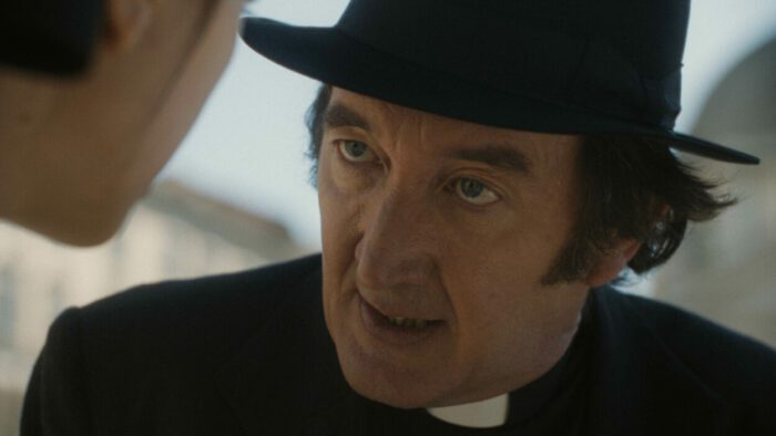 Ralph Ineson as Father Brennan in 20th Century Studios' THE FIRST OMEN. Photo courtesy of 20th Century Studios. © 2024 20th Century Studios. All Rights Reserved. Catholic priest in proper attire, black clothes and clerical tab collar, addressing Margaret.