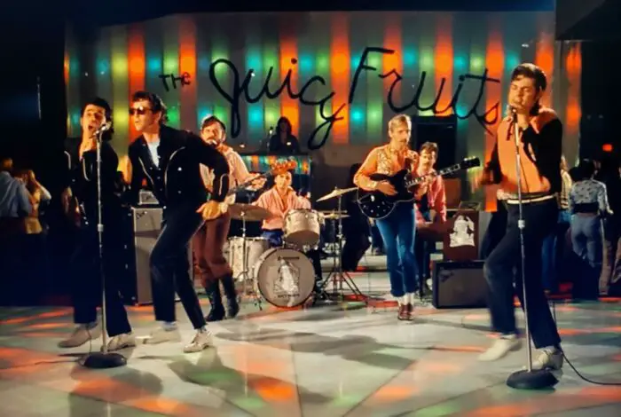 Fifties rockabilly style band featuring musicians dressed as greasers with slick pompadours and leather jackets.