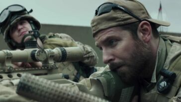 A man looks through a rifle scope next to his spotter in American Sniper