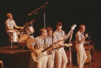 CALIFORNIA - CIRCA 1964: Rock and roll band "The Beach Boys" perform onstage in circa 1964 in California. (L-R) Dennis Wilson, Al Jardine, Carl Wilson, Brian Wilson, Mike Love. (Photo by Michael Ochs Archives/Getty Images). Photo of the Beach Boys performing on stage in their matching striped shirts.