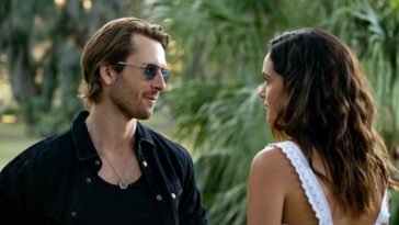 A man in sunglasses talks to a woman in a park in Hit Man.