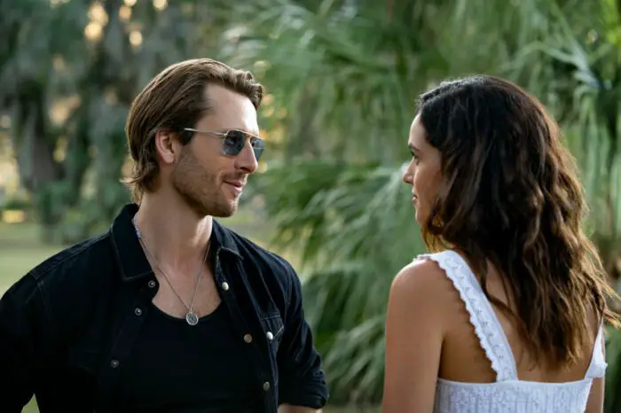 A man in sunglasses talks to a woman in a park.