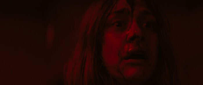 The young girl has blood on her face in red lighting