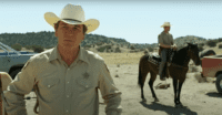 Sheriff Bell (Tommy Lee Jones) stands in the foreground surveying the massacre site while his deputy stands on horseback behind him