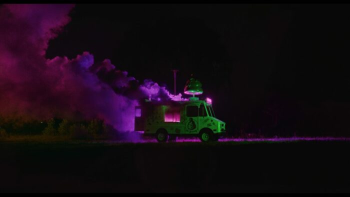A neon green truck emits pink smoke at night.