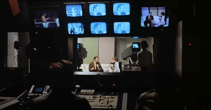 Robert Kerman as Prof. Harold Monroe and Enrico Papa as Pantheon interviewer in Cannibal Holocaust (1980). Screenshot off Peacock. Looking in at a television station control room as a news interviewer occurs featuring Prof. Monroe who has returned from the jungle.